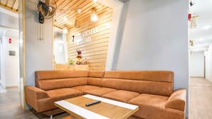 A modern hotel room with a large sectional sofa, a wooden coffee table, and a wall-mounted fan. - Fabhotel 7 Star (Surat)