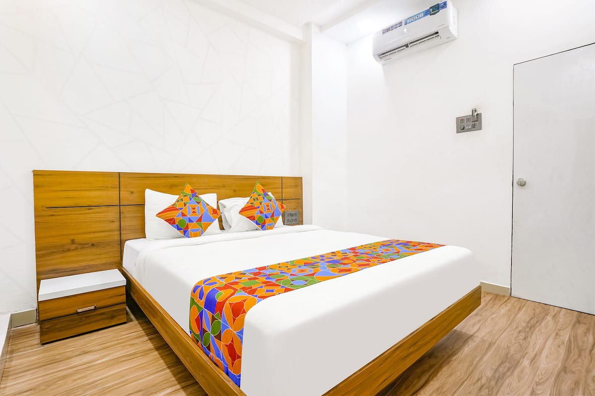A hotel room with a wooden headboard, a bed with colorful bedding, a nightstand, and a white door.