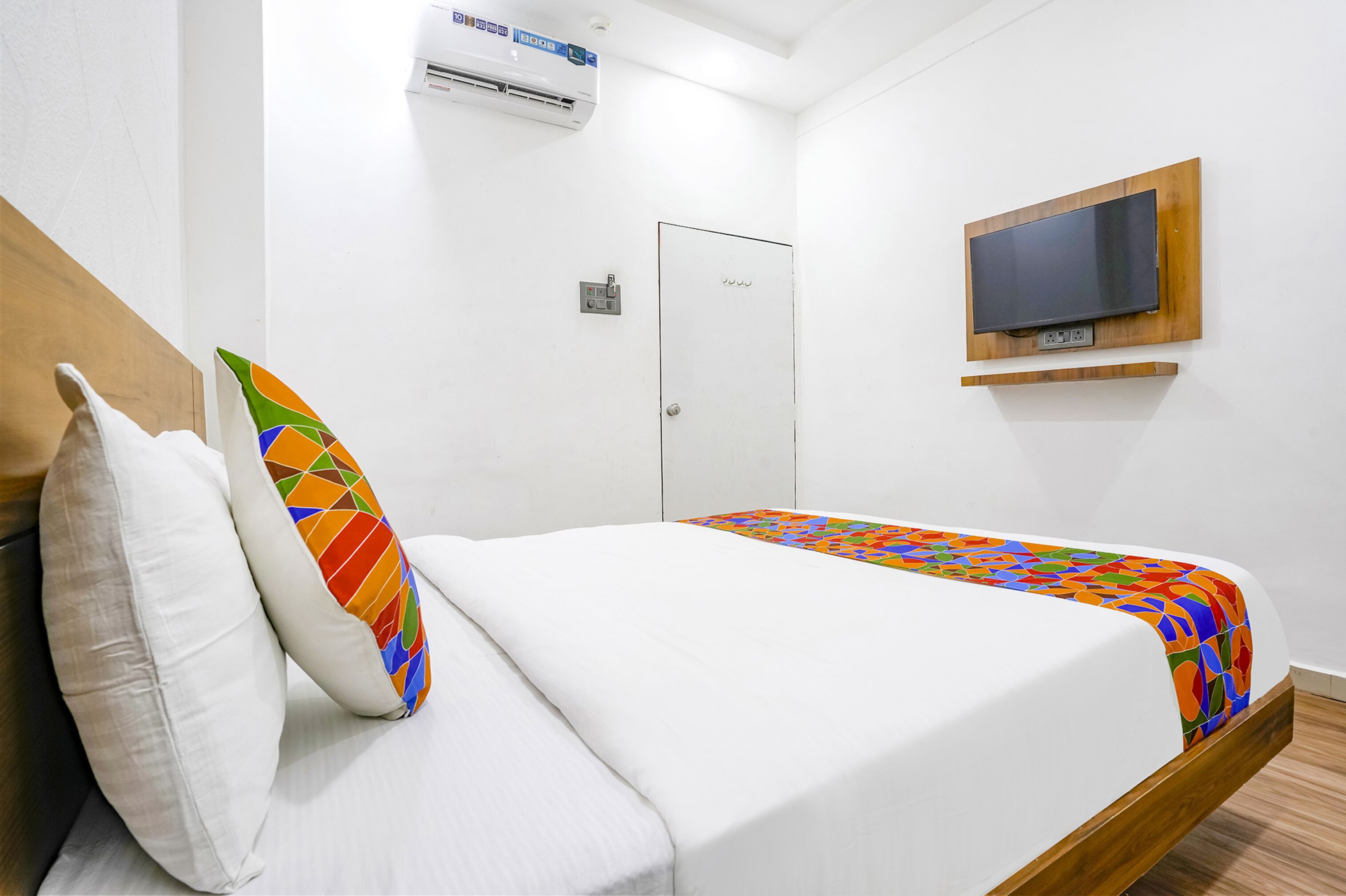 Una habitación de hotel con cama, televisor montado en la pared, aire acondicionado y una puerta.