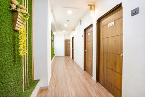 A corridor with wooden doors, a green wall with artificial grass, and a wooden bench with flowers. - Fabhotel 7 Star (Surat)