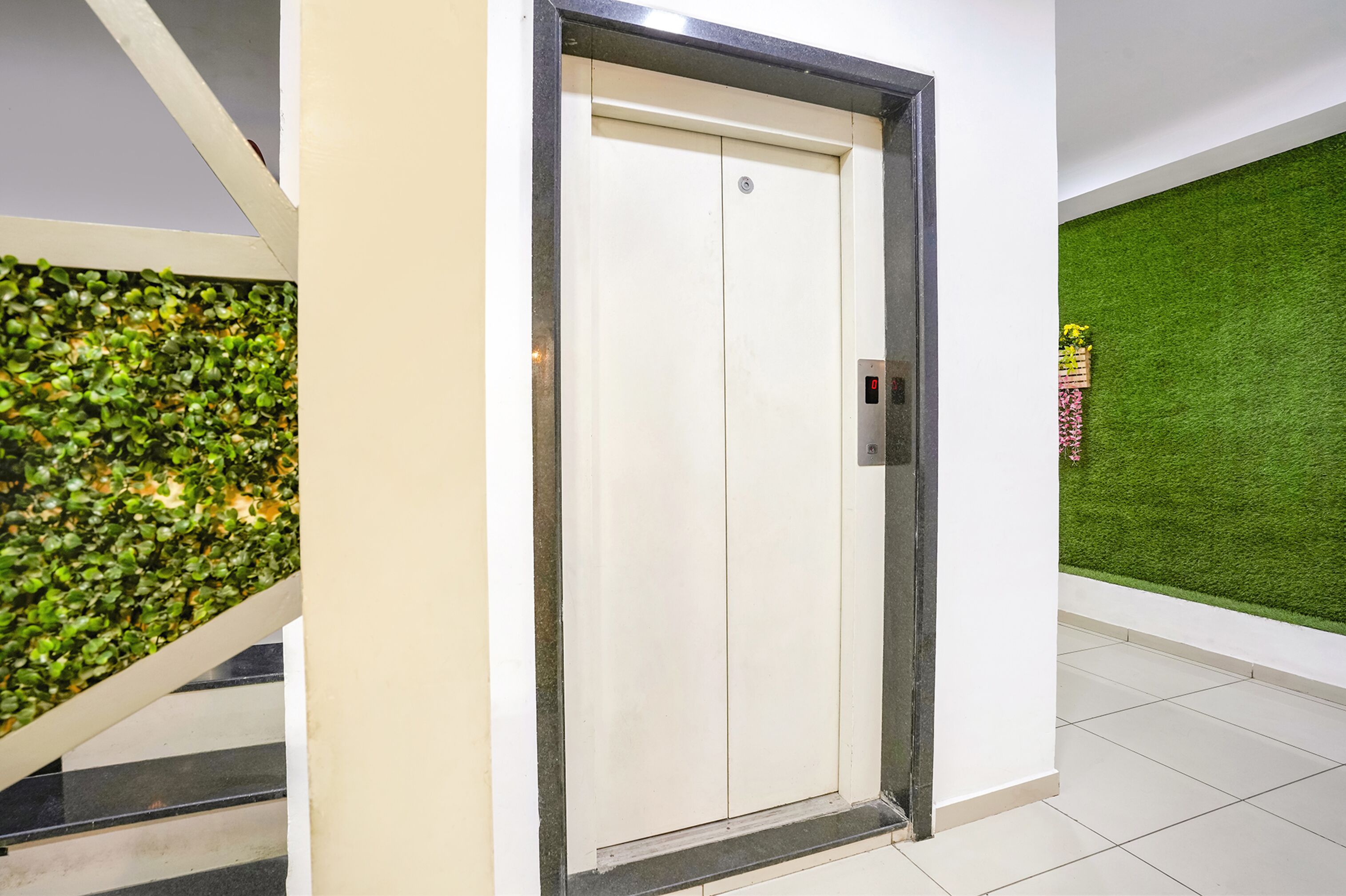 An elevator with a digital display, a green artificial grass wall, and a staircase with a green wall.