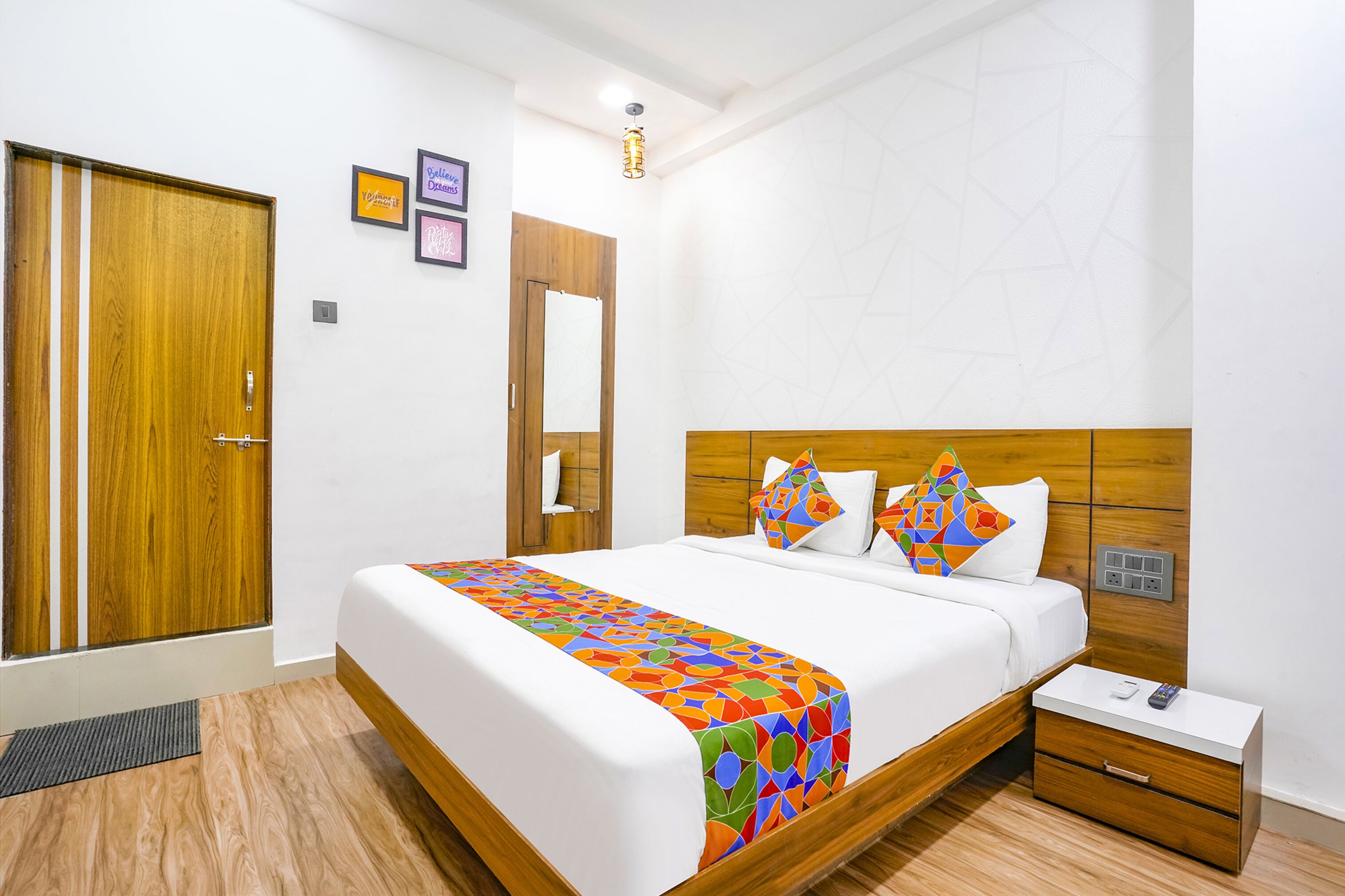 A modern hotel room with a wooden bed, a nightstand, a wardrobe, and a mirror.