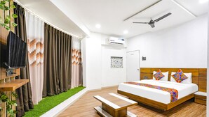 A modern bedroom with a wooden bed, a bedside table, a ceiling fan, and an air conditioning unit. - Fabhotel 7 Star (Surat)