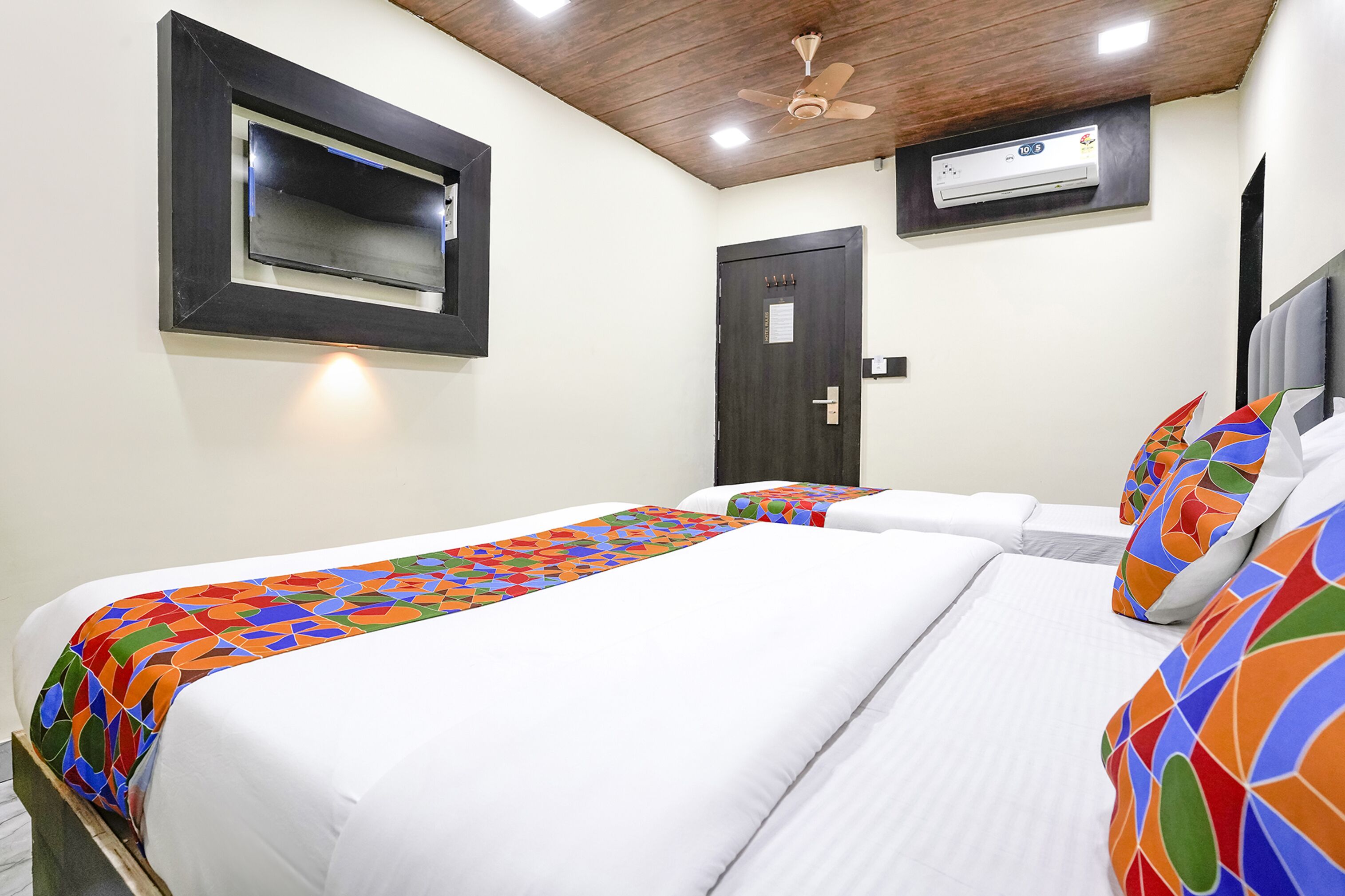 Ein Hotelzimmer mit zwei Betten, einem Deckenventilator, einer Klimaanlage und einer Tür mit Schloss.