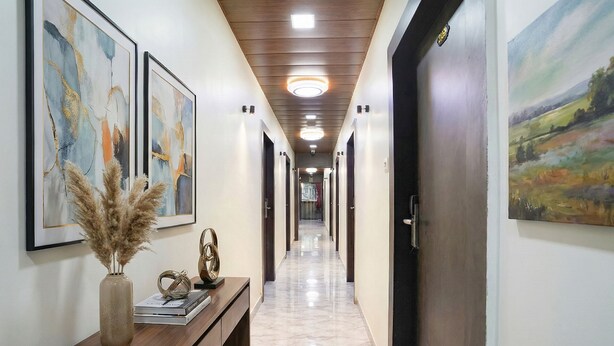 Un pasillo con obras de arte abstracto enmarcadas, una consola de madera con un jarrón y objetos decorativos, y un cuadro en la pared derecha.