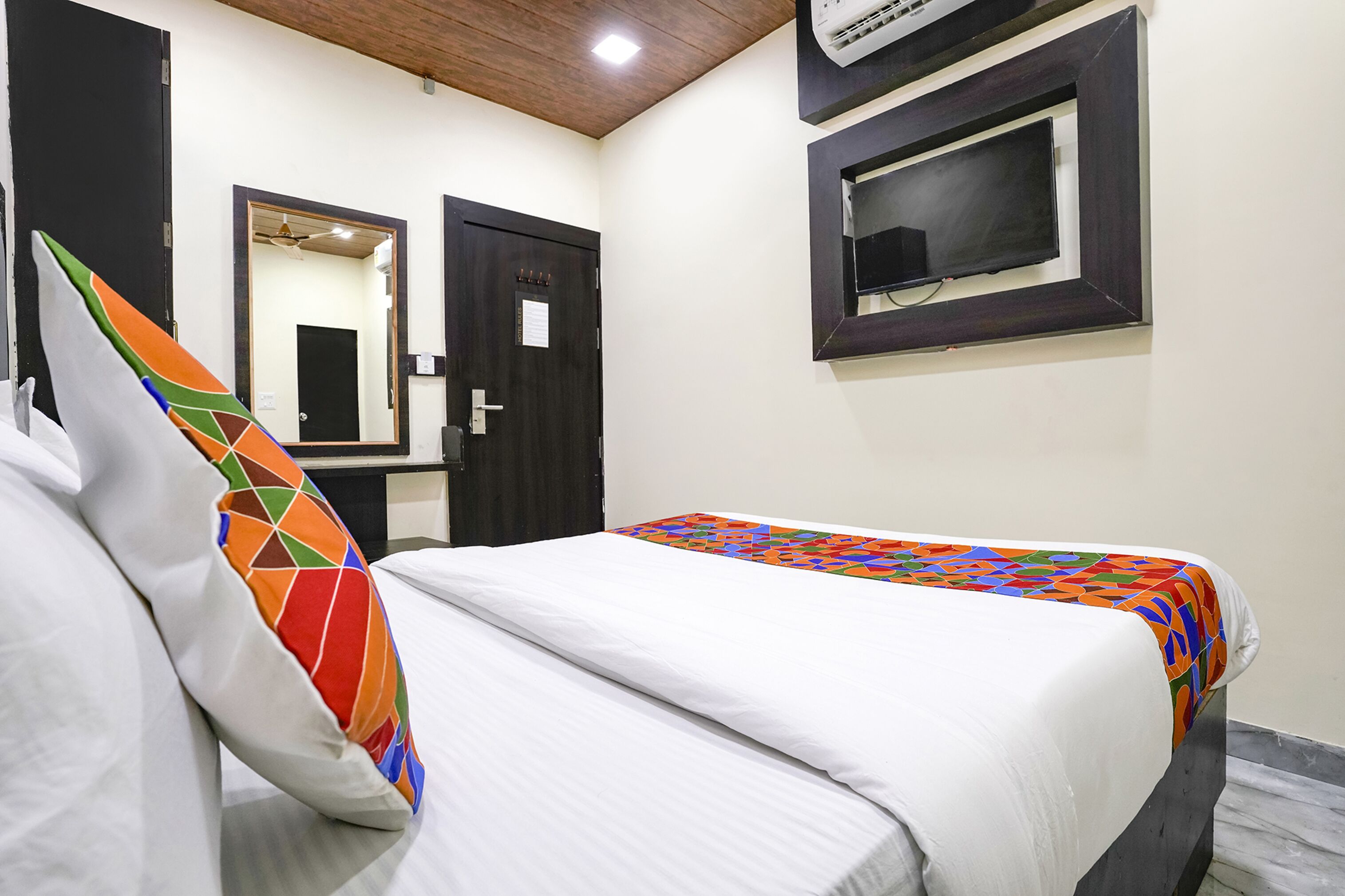 Quarto de hotel com cama, espelho, porta e aparelho de ar condicionado.