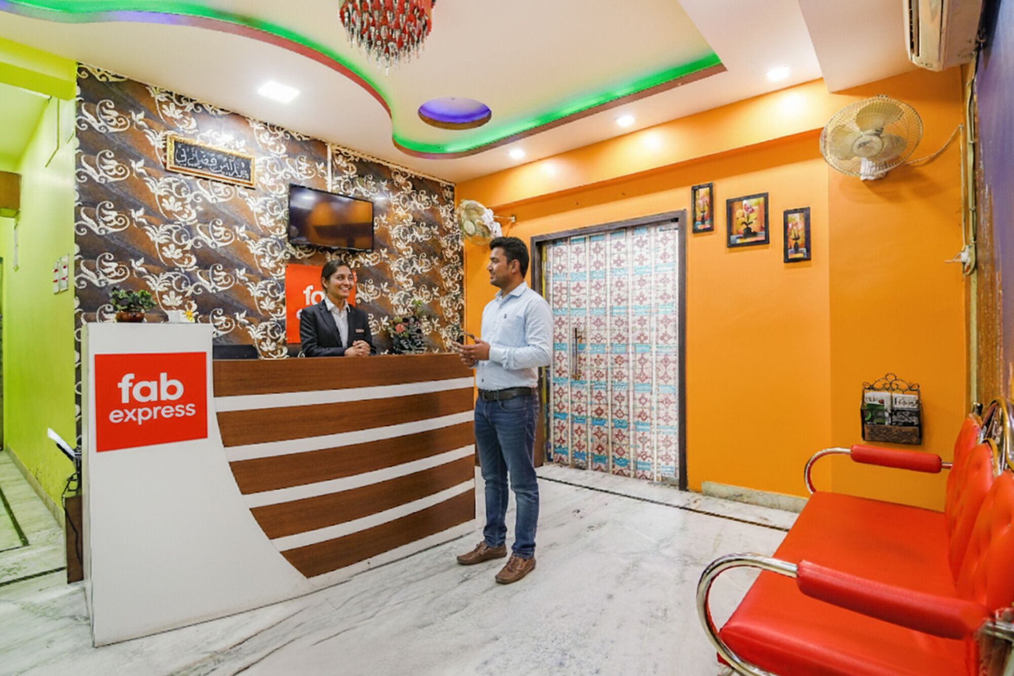 A reception area with a 'fab express' sign, a reception desk, a TV mounted on the wall, and a red chair.
