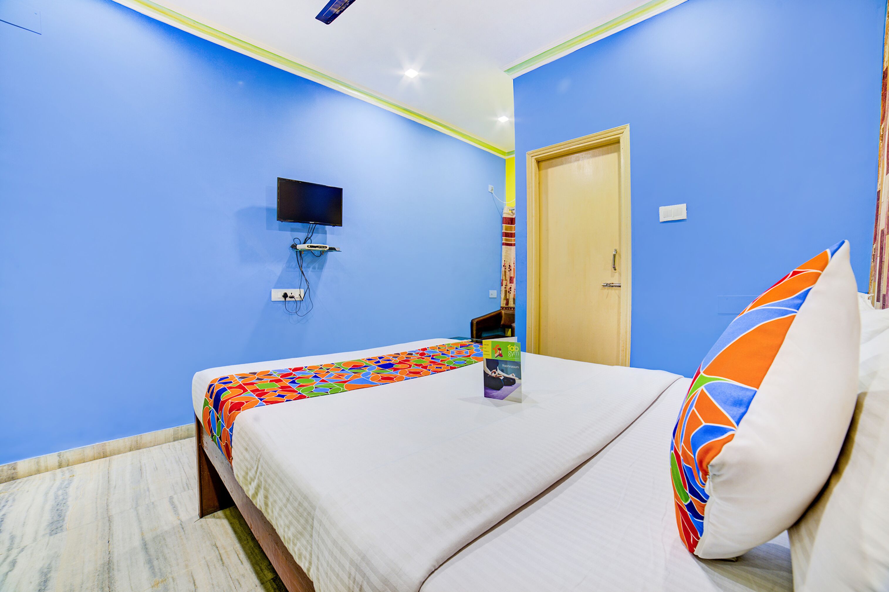 A hotel room with a bed, a TV mounted on the wall, and a door.