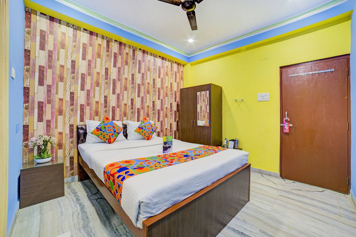 A hotel room with a bed, a ceiling fan, a wooden door, and a wall with a patterned curtain.