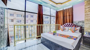 A hotel room with a large bed, a view of buildings through the window, and a balcony railing. - FabHotel Nest (Kolkata)
