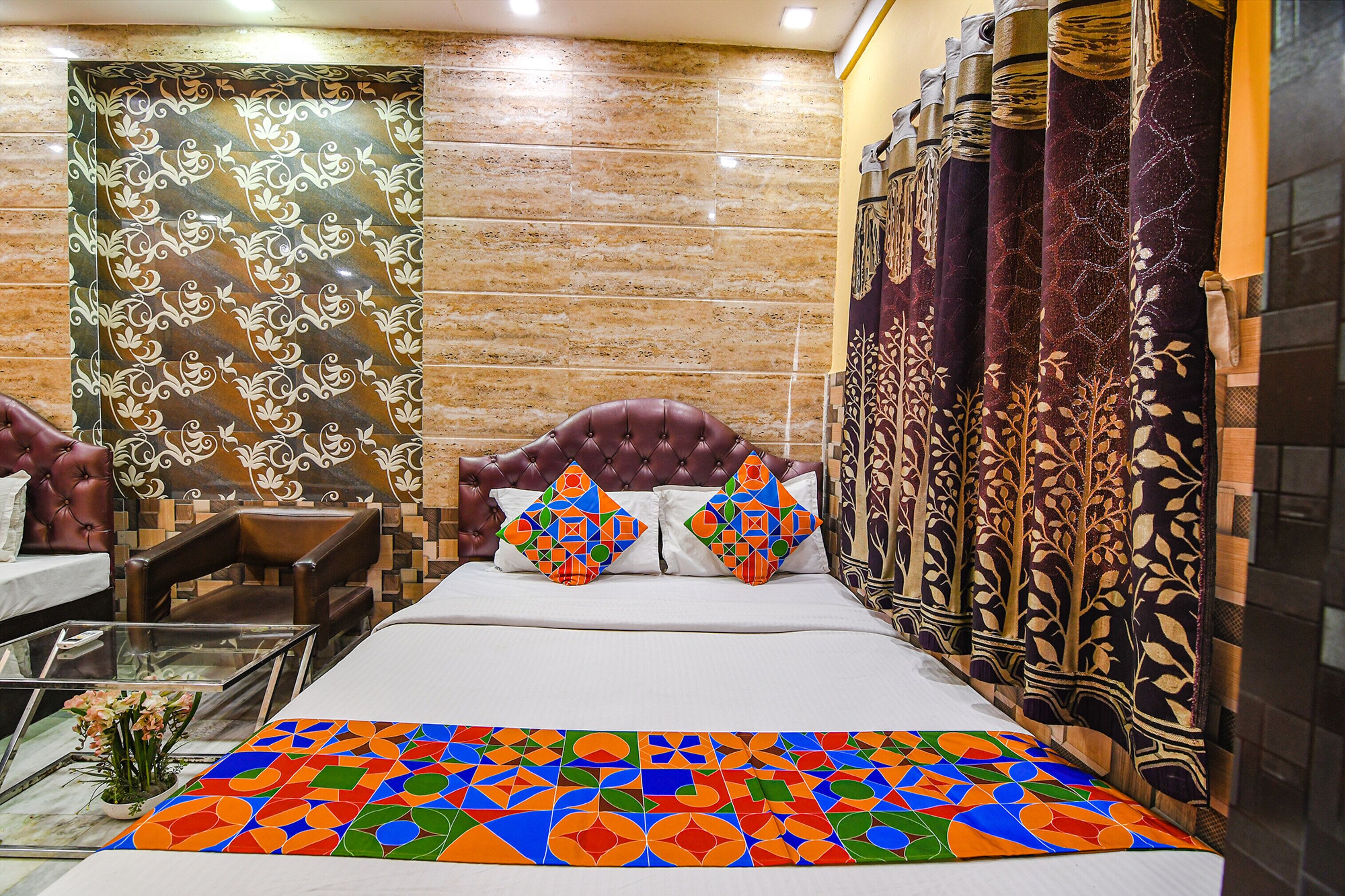 A hotel room with a bed, a brown leather chair, a glass coffee table, and a patterned wall.
