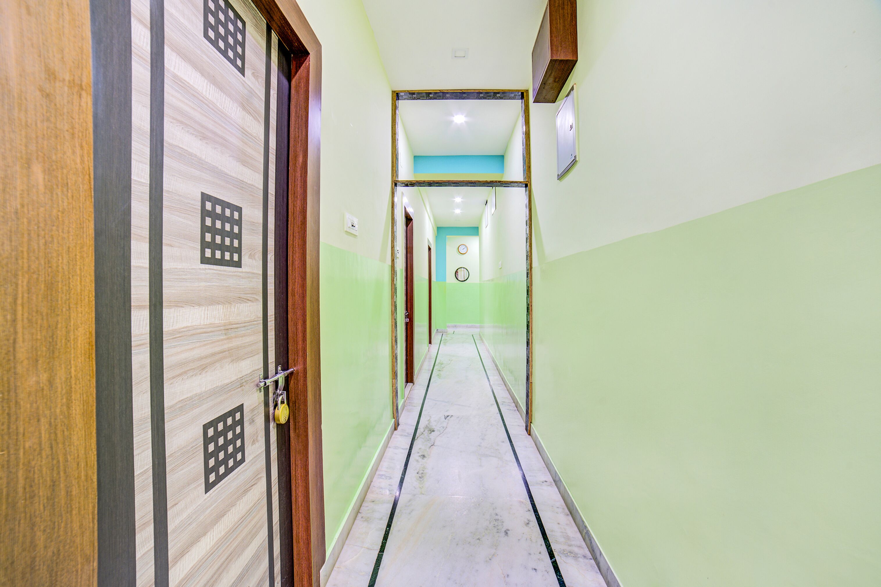 A corridor with a wooden door on the left, a tiled floor, and a green wall.