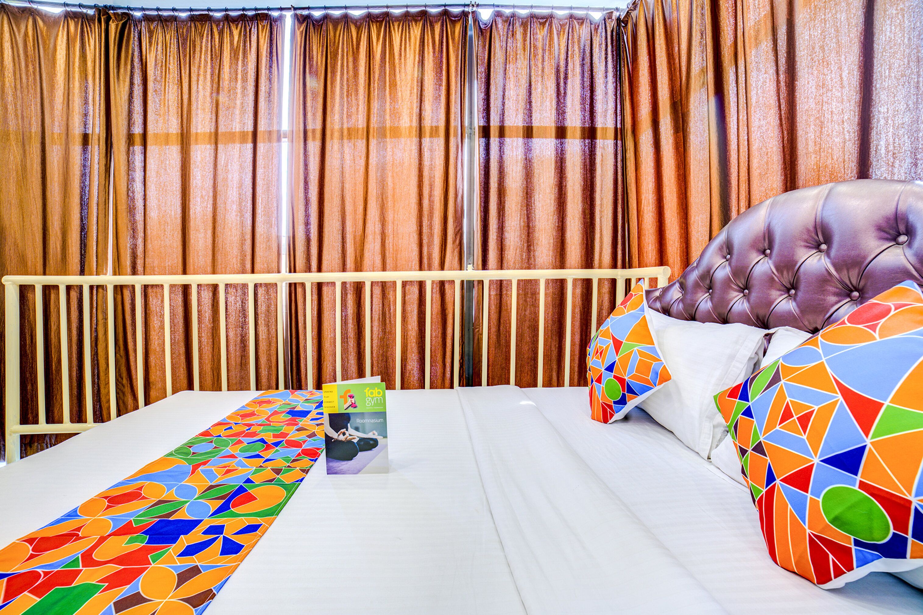 A hotel room with a bed, a colorful throw blanket, a pillow with a geometric pattern, and a book on the nightstand.