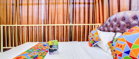A hotel room with a bed, a colorful throw blanket, a pillow with a geometric pattern, and a book on the nightstand.