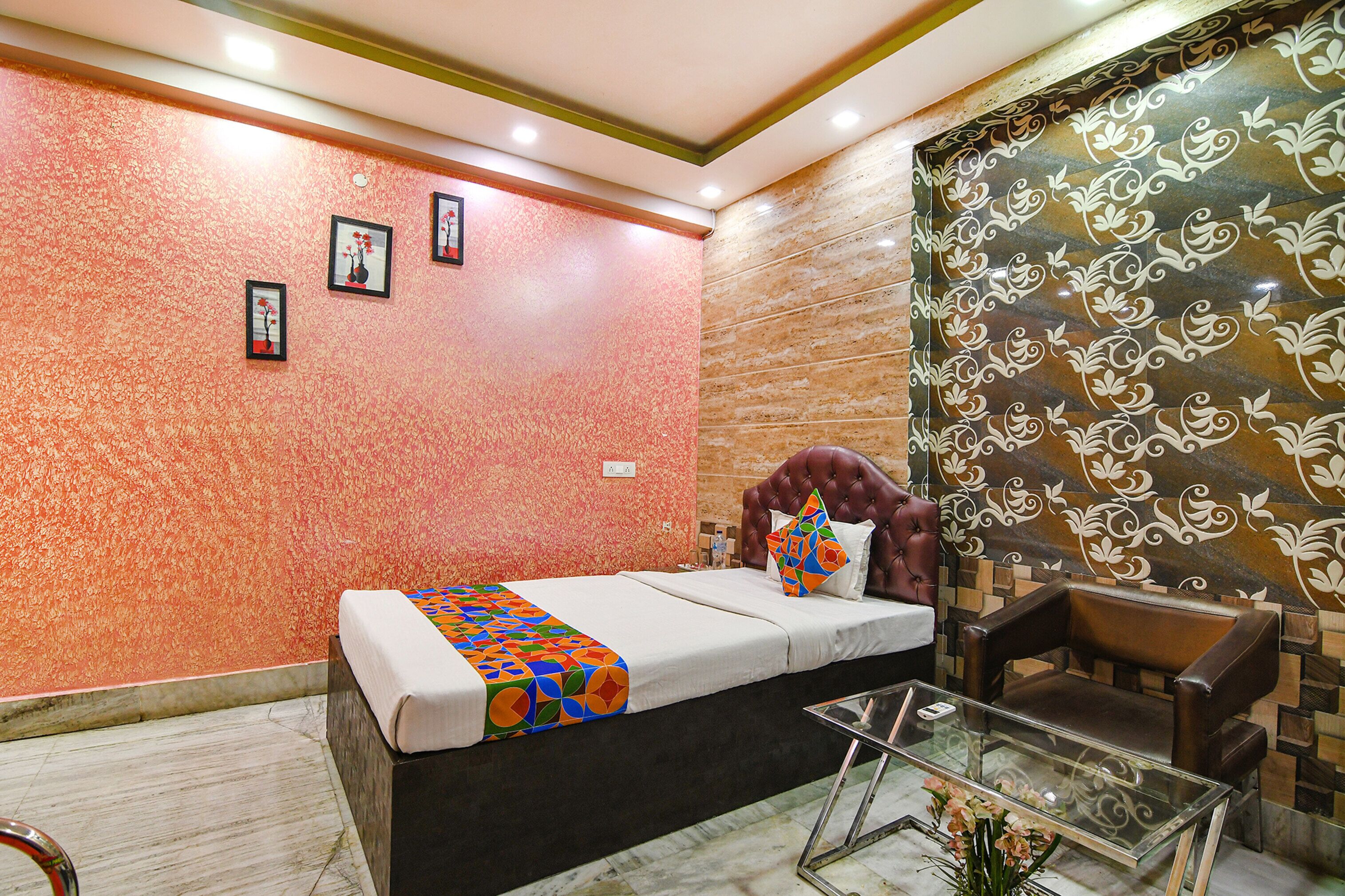 A hotel room with a bed, a glass coffee table, a leather armchair, and a decorative wall with a floral pattern.