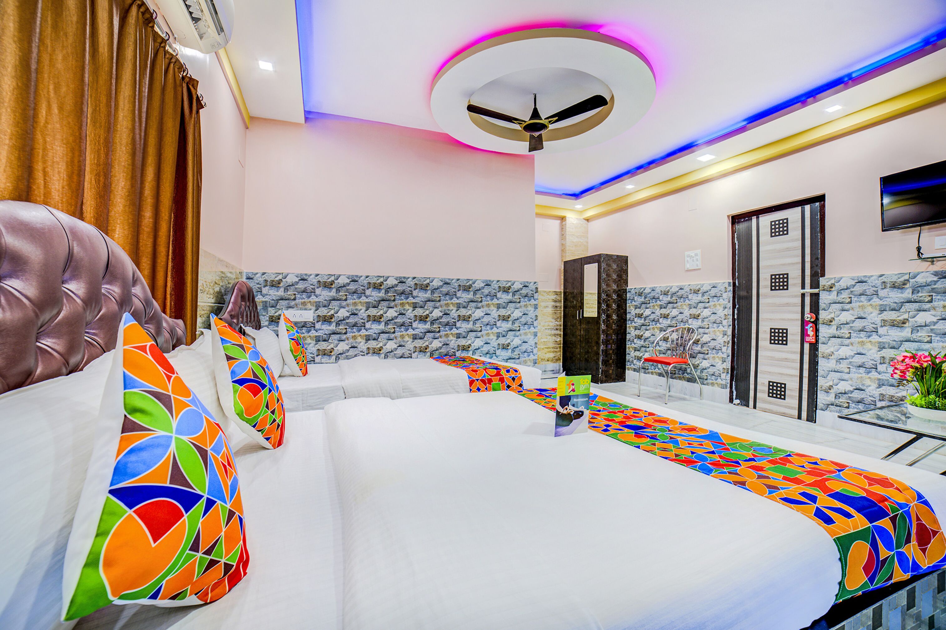 A hotel room with a bed, a ceiling fan, a TV, and a stone-patterned wall.