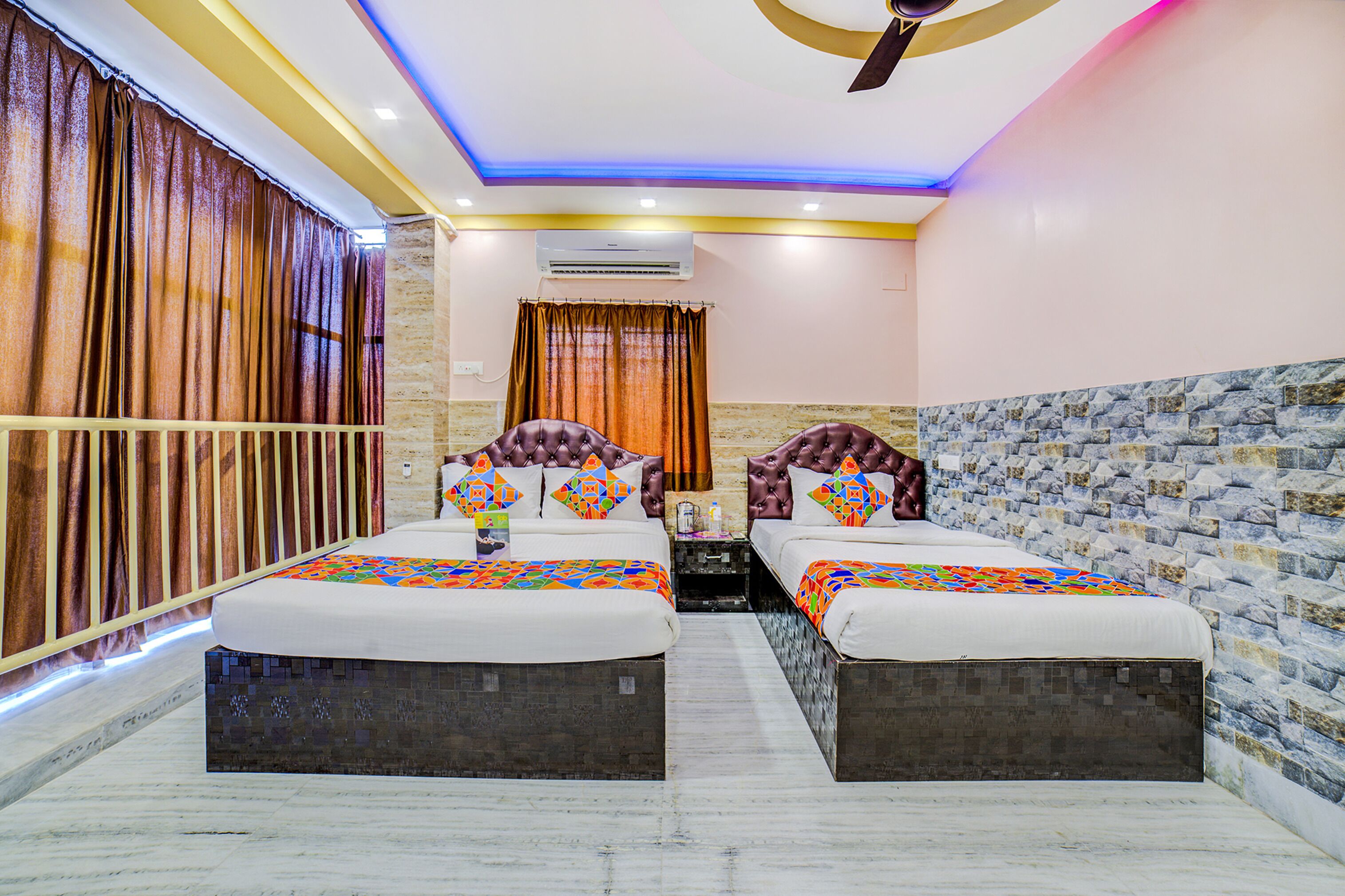A hotel room with two beds, a ceiling fan, an air conditioning unit, and a patterned wall.