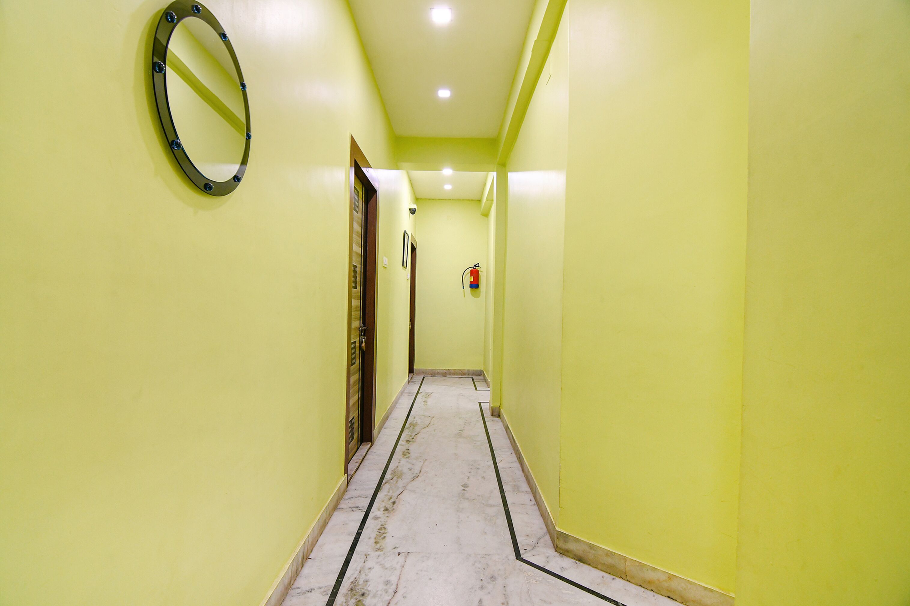 A narrow hallway with yellow walls, a marble floor, and a round mirror on the left.