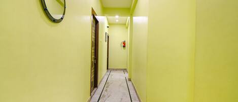 A narrow hallway with yellow walls, a marble floor, and a round mirror on the left.