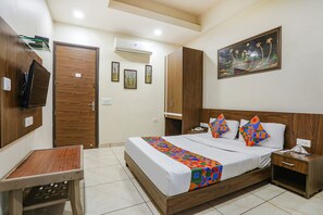 A hotel room with a bed, bedside table, nightstand, TV, wardrobe, and artwork on the wall. - Fabexpress City Heart (New Delhi)