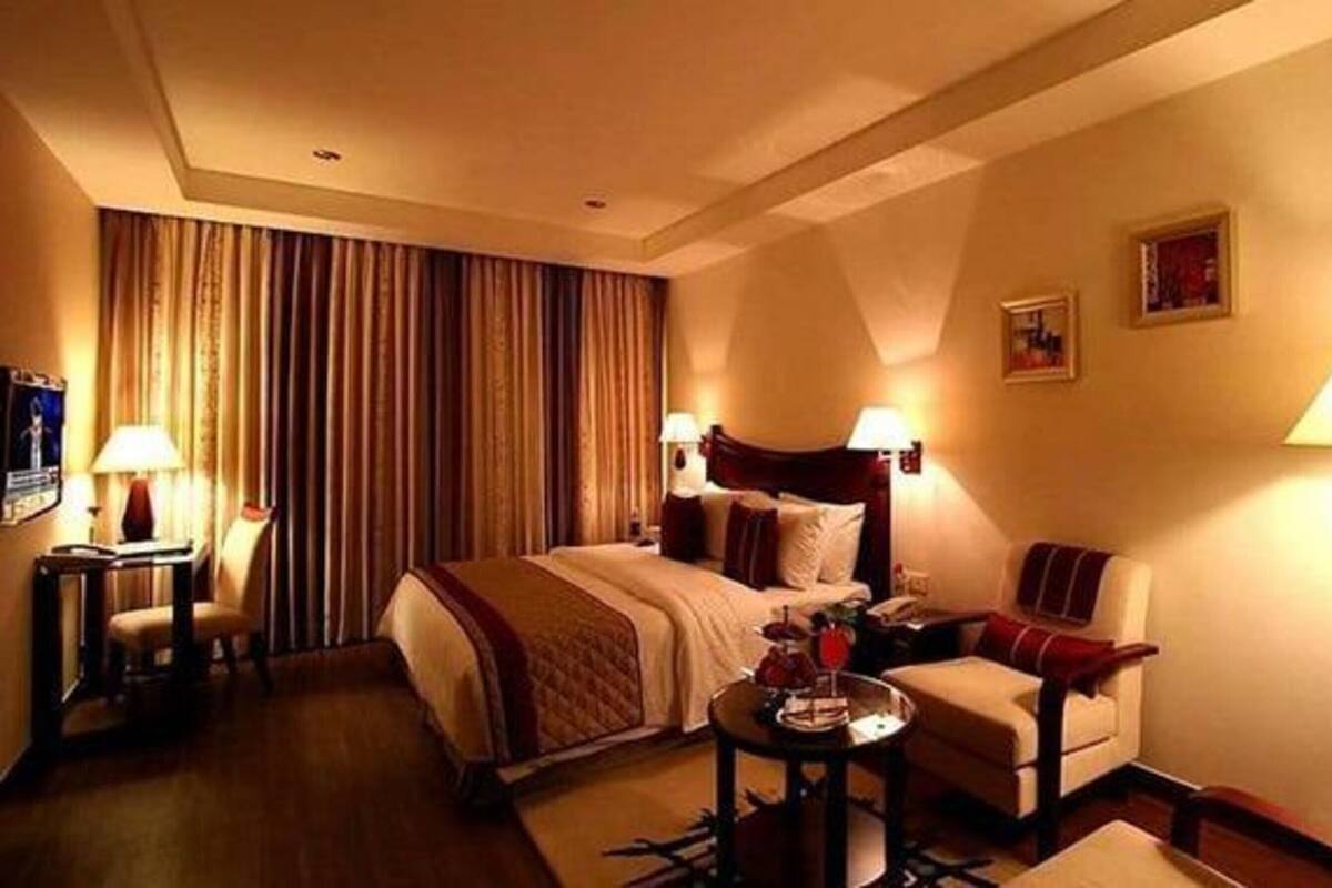 Quarto de hotel com uma cama grande, duas mesas de cabeceira com luminárias, um sofá e uma pequena mesa redonda.