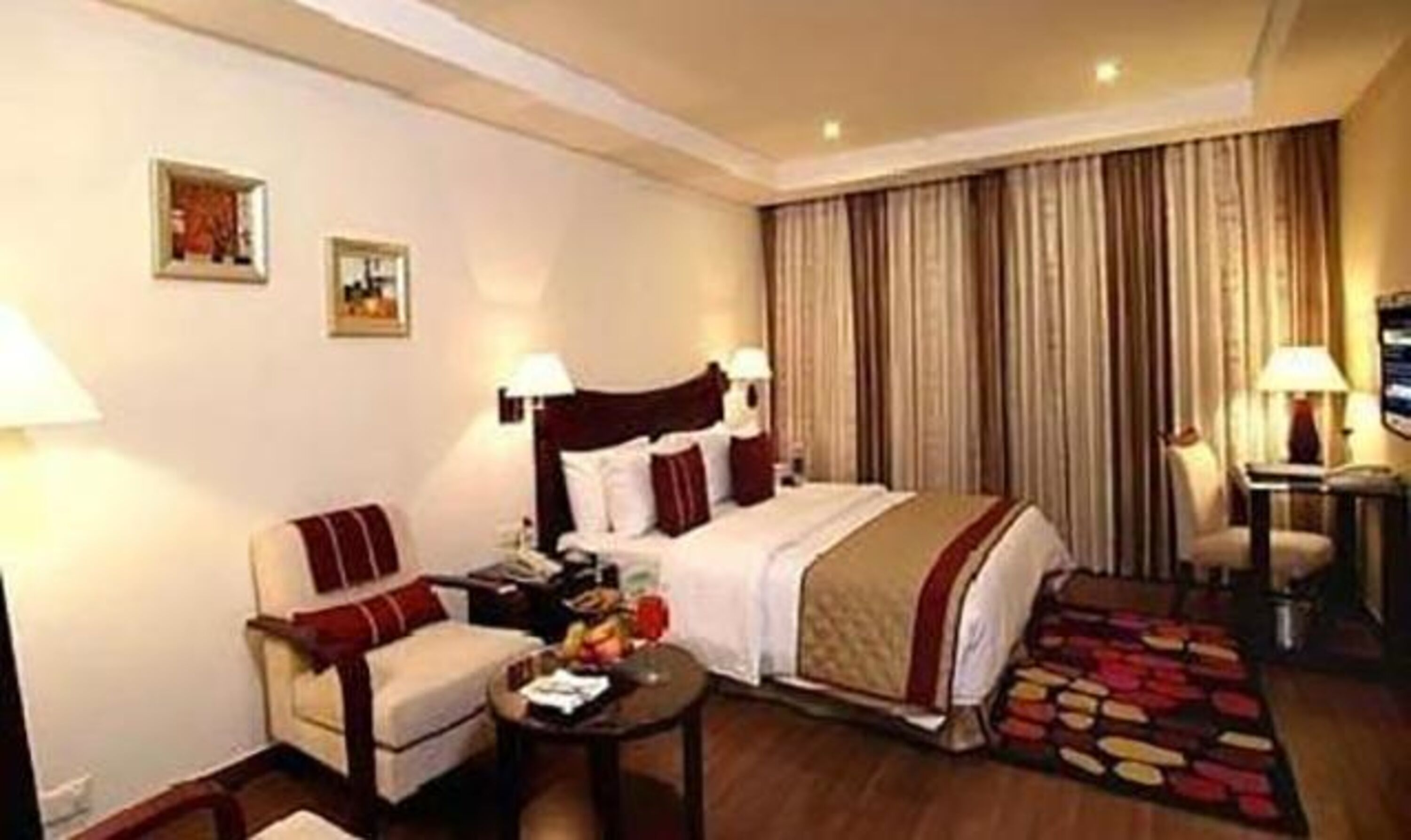 A hotel room with a bed, a chair, a small table, and a desk with a lamp.