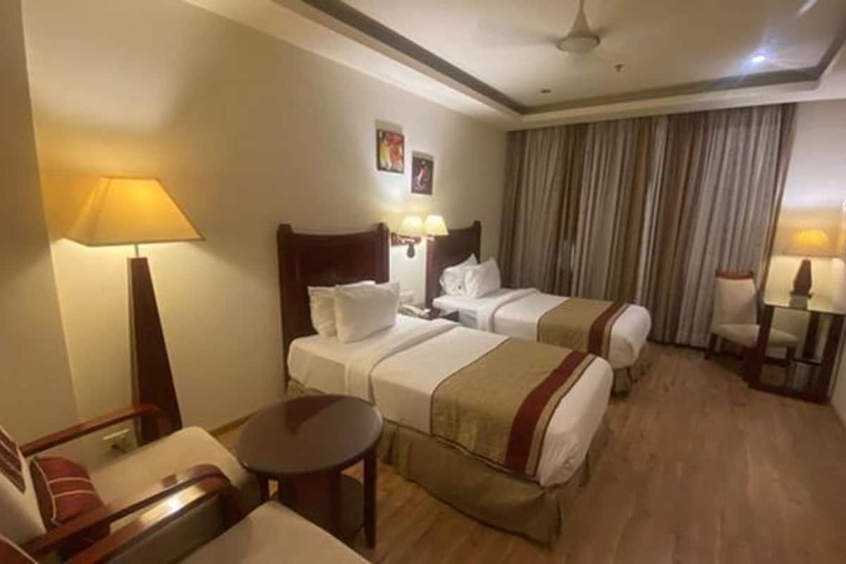 Quarto de hotel com duas camas, uma escrivaninha, uma cadeira e uma televisão.