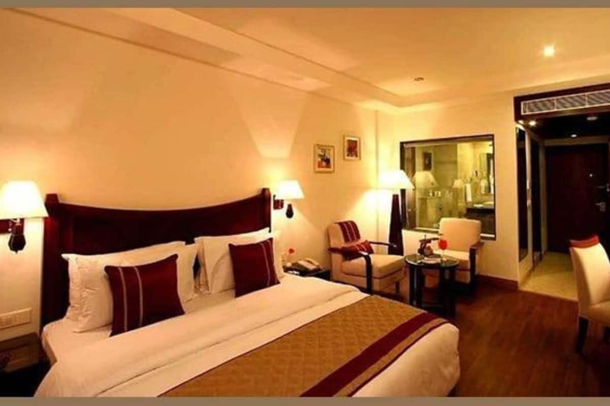 Quarto de hotel com uma cama grande, duas mesas de cabeceira, uma escrivaninha, uma cadeira e um espelho.