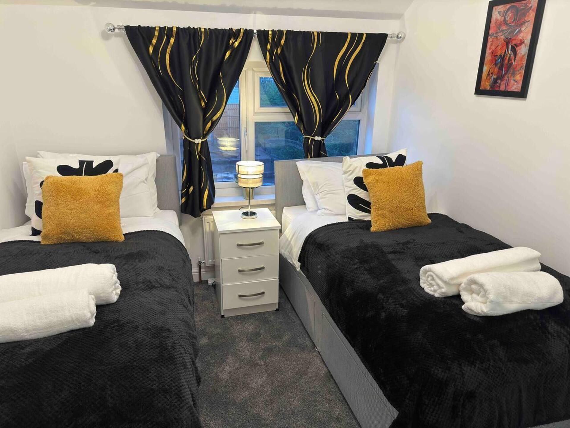 A hotel room with two beds, a bedside table, a lamp, and a window with curtains.