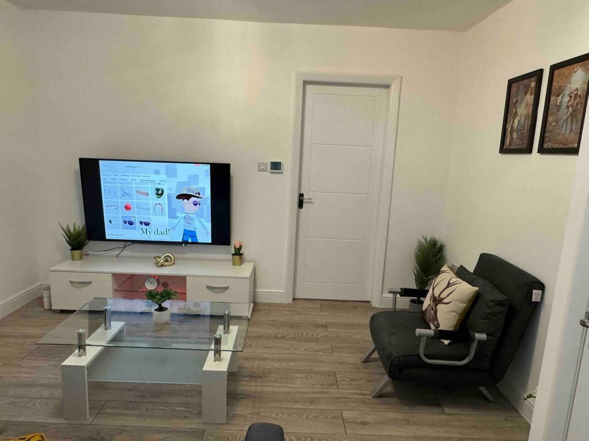 Una sala de estar moderna con una televisión de pantalla plana, una mesa de centro de vidrio, un sofá y una puerta.