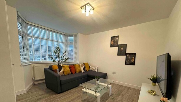 A modern living room with a sectional sofa, a glass coffee table, and a flat-screen TV on a stand. - 3-bed Home, Sleeps 8, Ideal for Large Groups (Birmingham)
