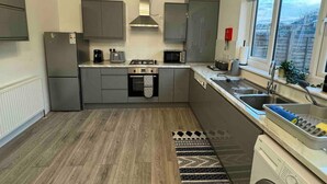 A compact kitchen with grey cabinets, a built-in oven, a microwave, and a sink. - 3-bed Home, Sleeps 8, Ideal for Large Groups (Birmingham)