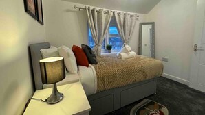 A bedroom with a bed, bedside table, lamp, and a view of the outside. - 3-bed Home, Sleeps 8, Ideal for Large Groups (Birmingham)