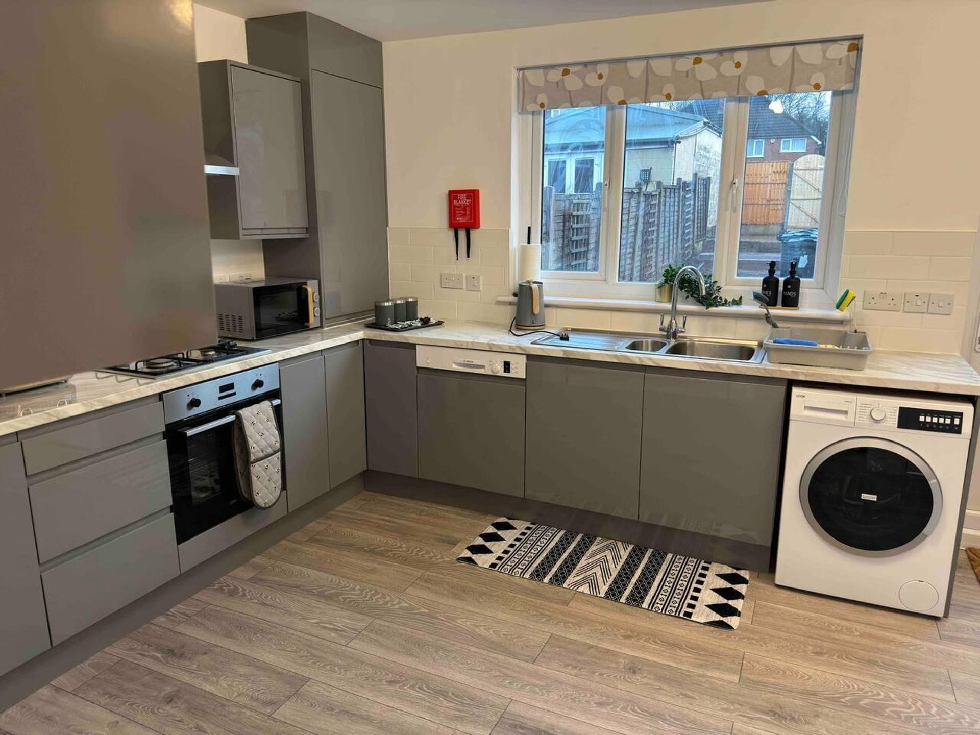 A modern kitchen with grey cabinets, a built-in microwave, a stove, a sink, and a washing machine.