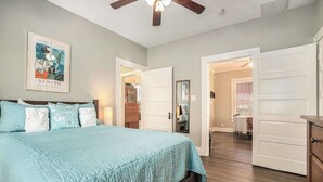 Un dormitorio con cama, ventilador de techo y puerta que da a otra habitación.