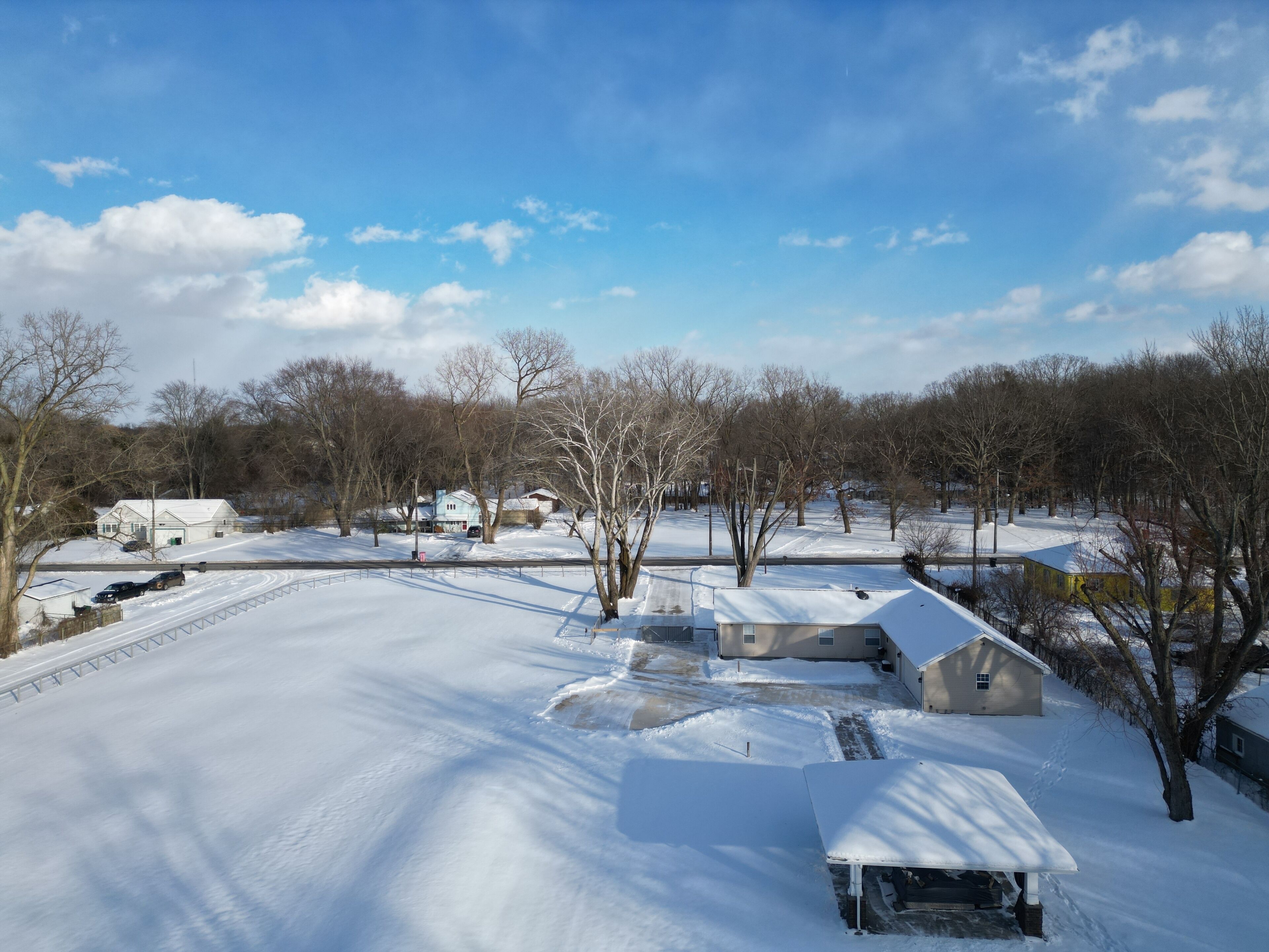 A snow-covered residential area with houses, a road, and trees.