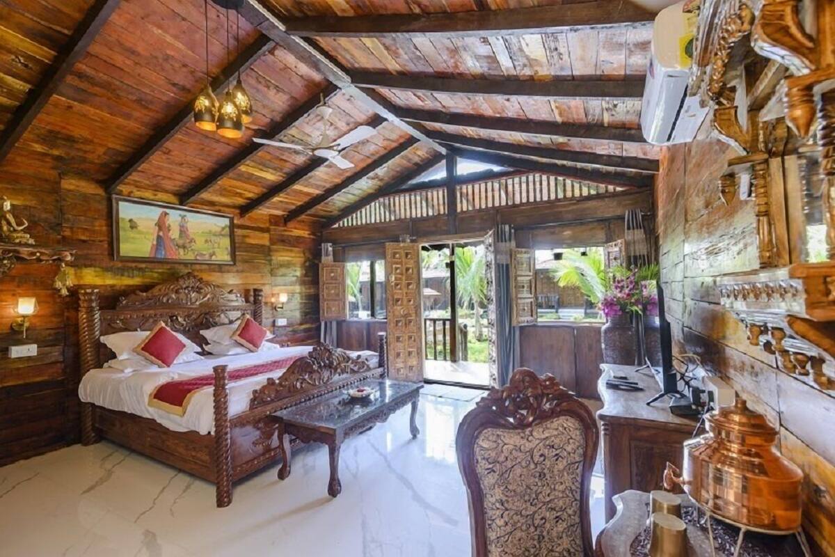 Une pièce en bois avec un lit, une table et une chaise. Il y a un tableau au mur et une fenêtre donnant sur un paysage verdoyant.
