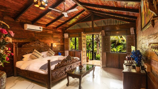 A wooden room with a bed, a table, and a ceiling fan. - Little Cove Nature Resort (Nashik)