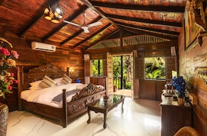 A wooden room with a bed, a table, and a ceiling fan. - Little Cove Nature Resort (Nashik)
