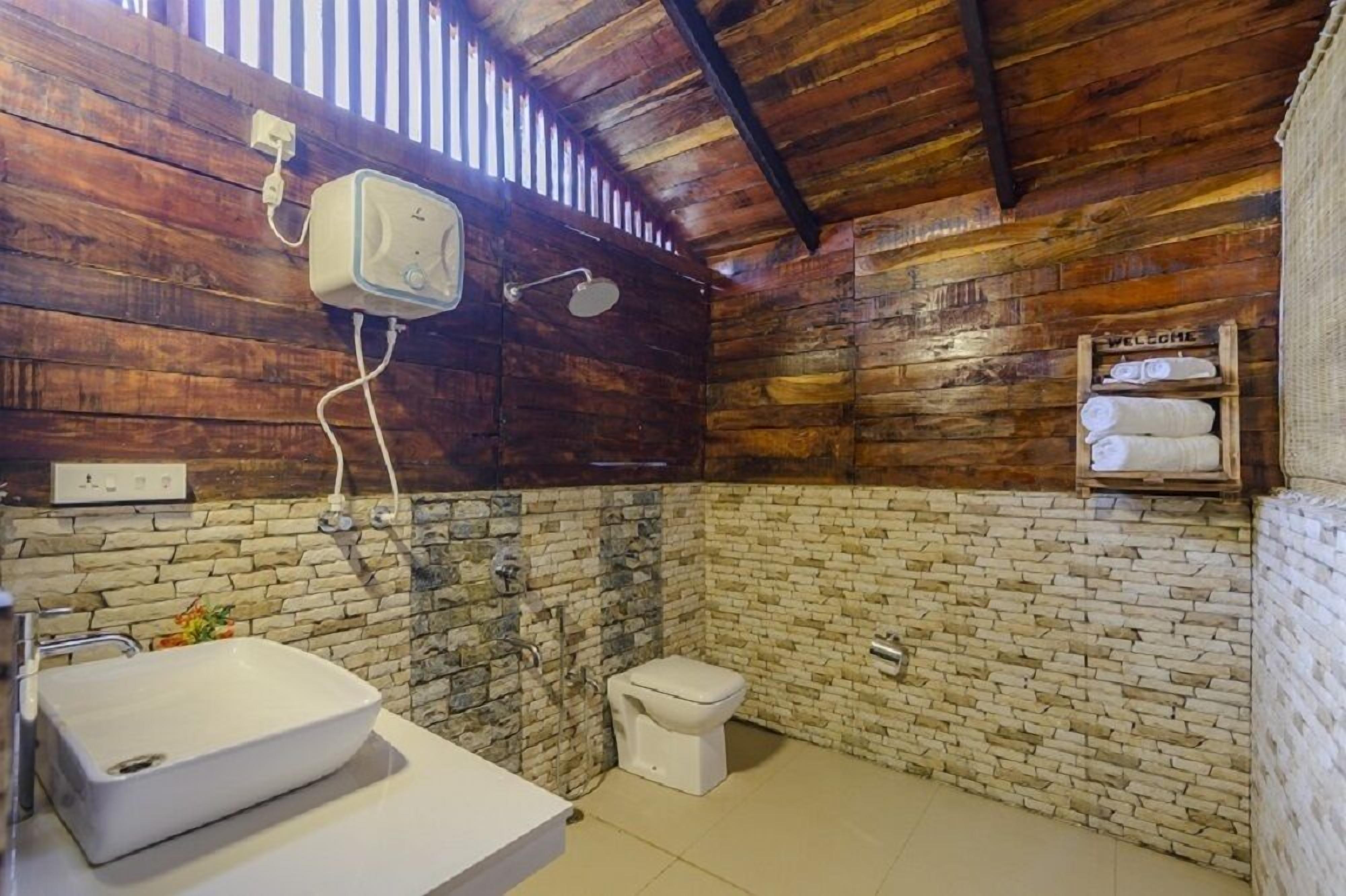 Un baño rústico con pared de piedra, techo de madera, un lavamanos blanco y un inodoro.