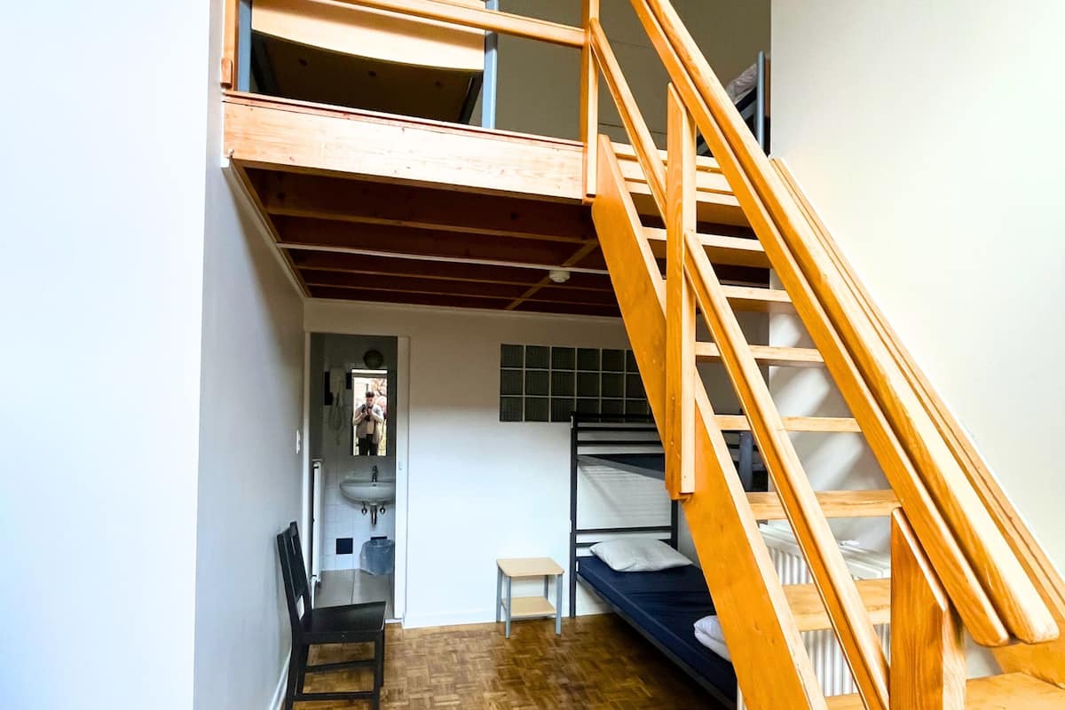 A room with a bunk bed, a wooden staircase, a small table, and a chair.