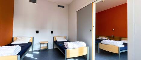 A hotel room with three single beds, a small table, and a sliding door leading to another room.