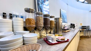 A breakfast buffet with various food containers, a coffee machine, and a tray with a sandwich and a cup. - Hostel van Gogh (Brussels)