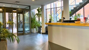 A reception area with a wooden counter, glass doors, potted plants, and a staircase leading to an upper level. - Hostel van Gogh (Brussels)