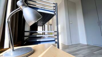 A bunk bed with a desk lamp, a wooden table, and a grey wardrobe in a room with a light-colored floor.