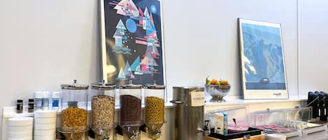 Una zona de bufé con distintos dispensadores de comida, un bol de fruta y dos cuadros en la pared.