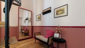 Una habitación con cama, una silla, una mesita, un espejo y cuadros en la pared.