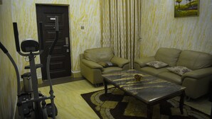A living room with a sofa, a coffee table, and an exercise bike. - UG Wils Hotels and Suites  (Calabar)
