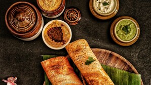 Two rolled flatbreads on a wooden plate with a banana leaf underneath, accompanied by small bowls of chutney and sauces. - Grand Auli Camp (Joshimath)