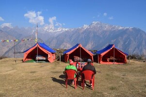 Tres tiendas de campaña rojas con techos azules, frente a un telón de fondo de montañas nevadas.